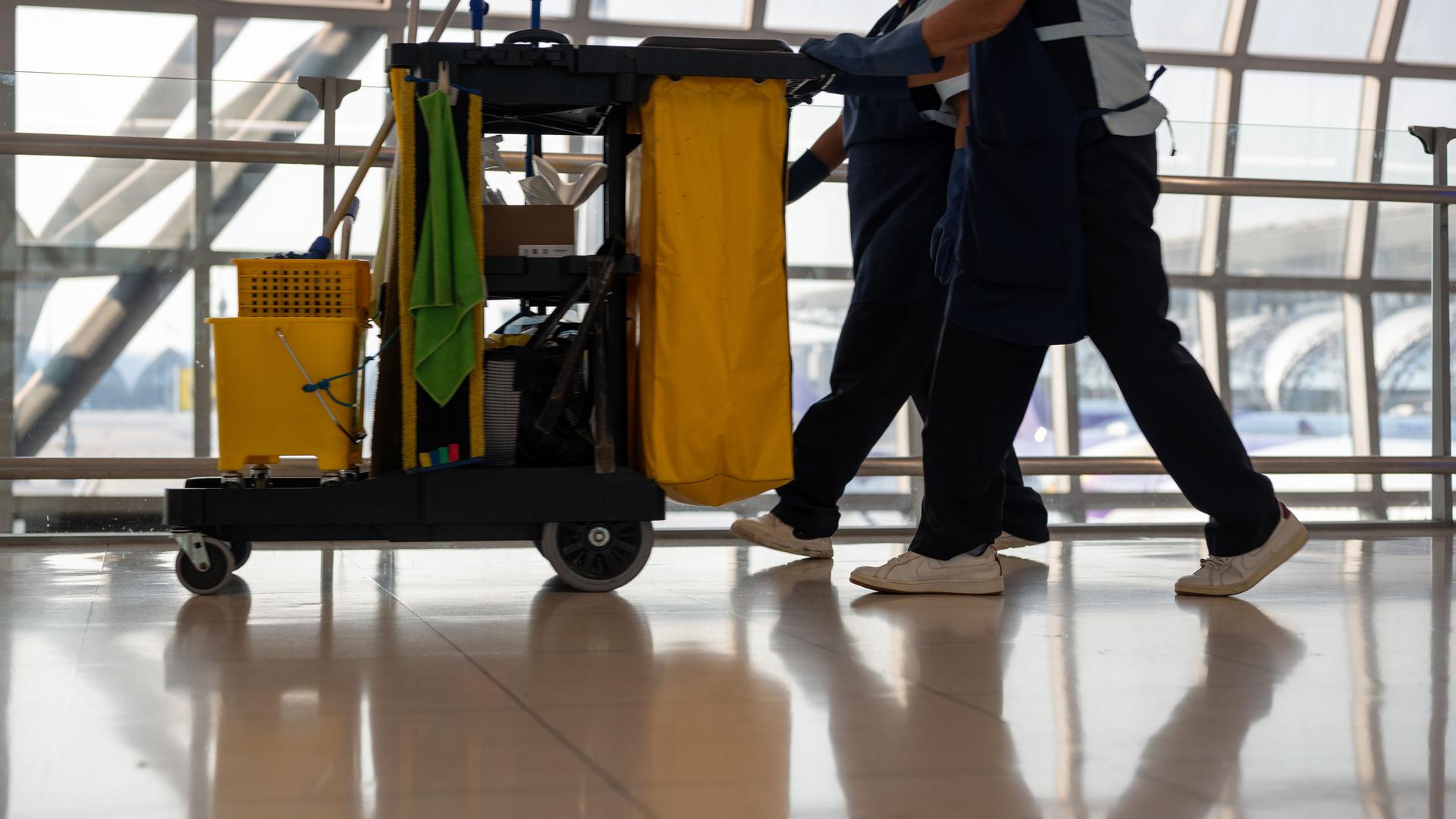 cleaners working in passenger airport terminal pushing trolley with cleaning stuffs
